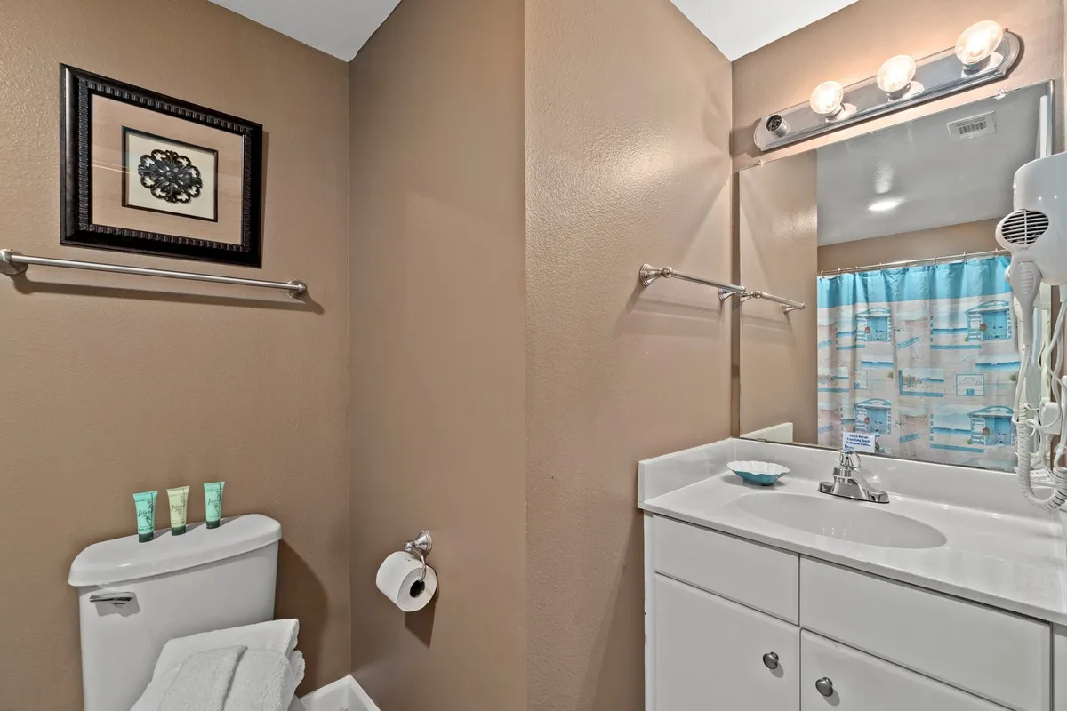 A practical, clean bathroom with a white vanity and large mirror, beach-themed shower curtain, and mounted hairdryer. The space is tidy, functional, and designed for convenience, making it ideal for families and groups managing daily routines.