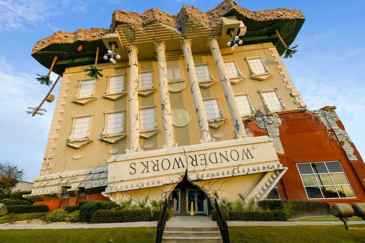 The whimsical, upside-down building of WonderWorks stands out with its large, ornate columns and playful architecture. The inverted signage and entrance hint at the interactive attractions and fun experiences inside.